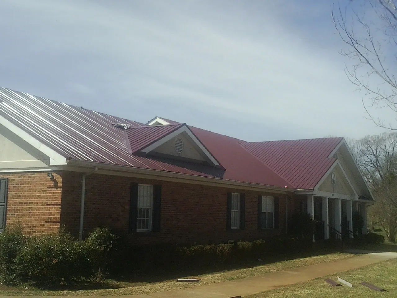 Red metal roof with gabled entries on a long brick building, from a Hail Damage Roof Repair job in Barberton