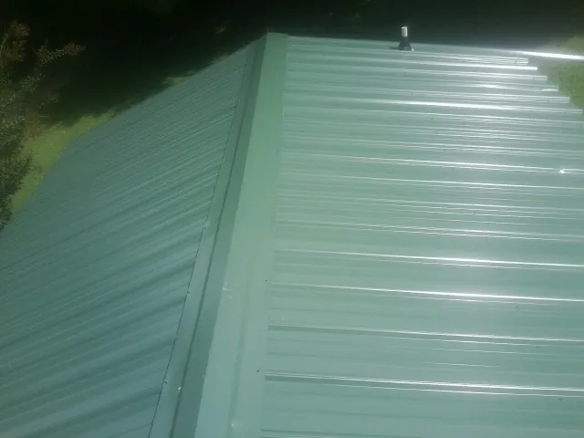 New green metal panels meeting at the ridge of a roof — Flat Roof Repair work by our crew in Barberton