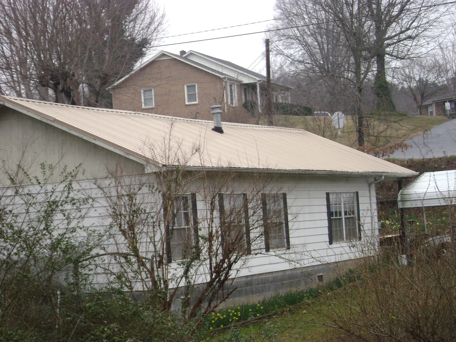Tan metal roof on a white sided house set into a hillside — Commercial Roofing by Roofing Brothers in Barberton