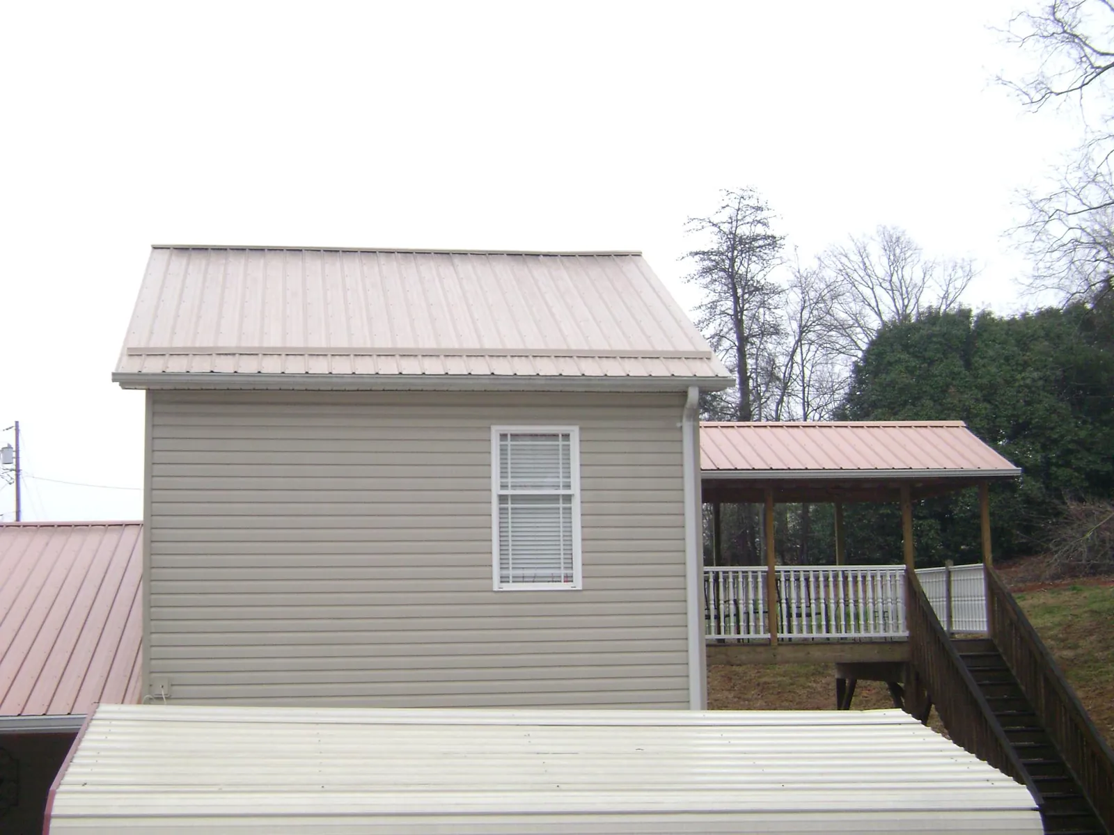 Tan metal roofs on a two story addition and attached porch, from a Roof Replacement job in Barberton